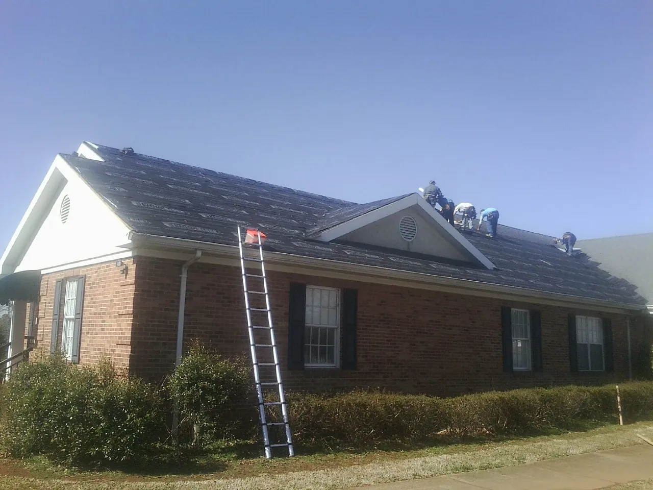 Crew tearing shingles off a brick ranch roof with a ladder set — Emergency Roof Repair work by our crew in South Thomaston