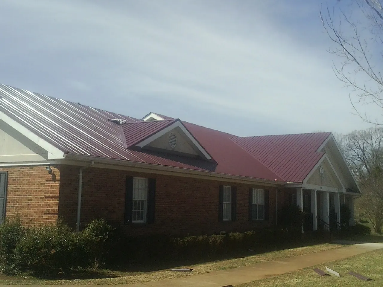 Red metal roof with gabled entries on a long brick building, from a Hail Damage Roof Repair job in South Thomaston