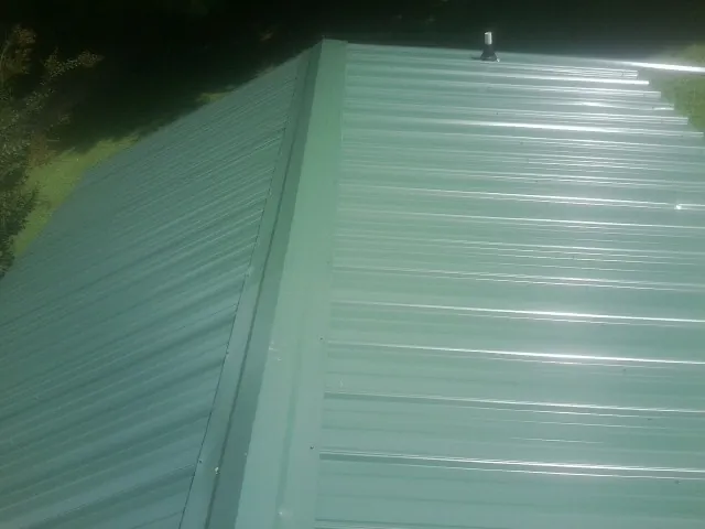 New green metal panels meeting at the ridge of a roof — Flat Roof Repair work by our crew in South Thomaston