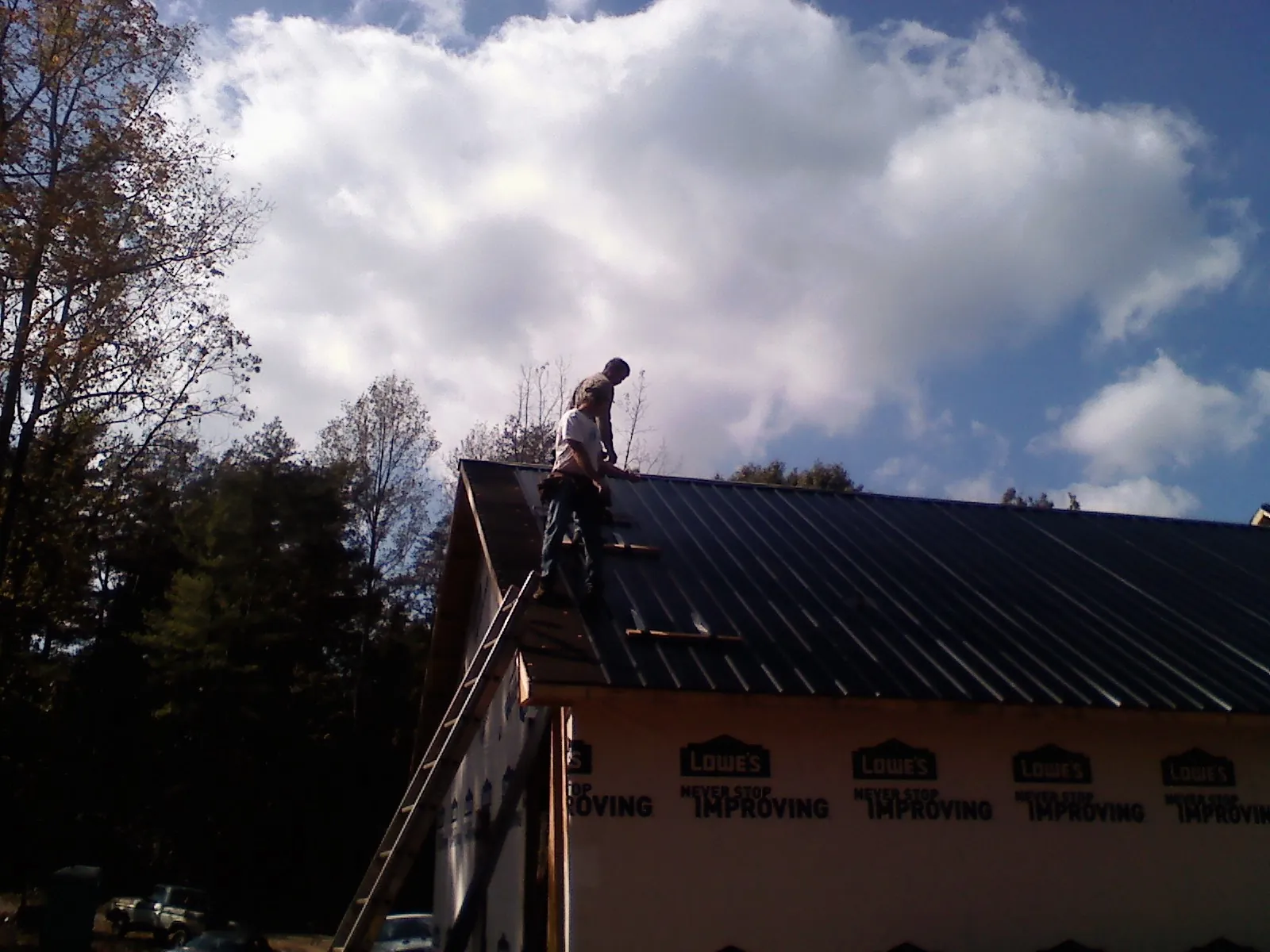 Roofer fastening dark metal panels high against a cloudy sky, from a Roof Inspection job in South Thomaston