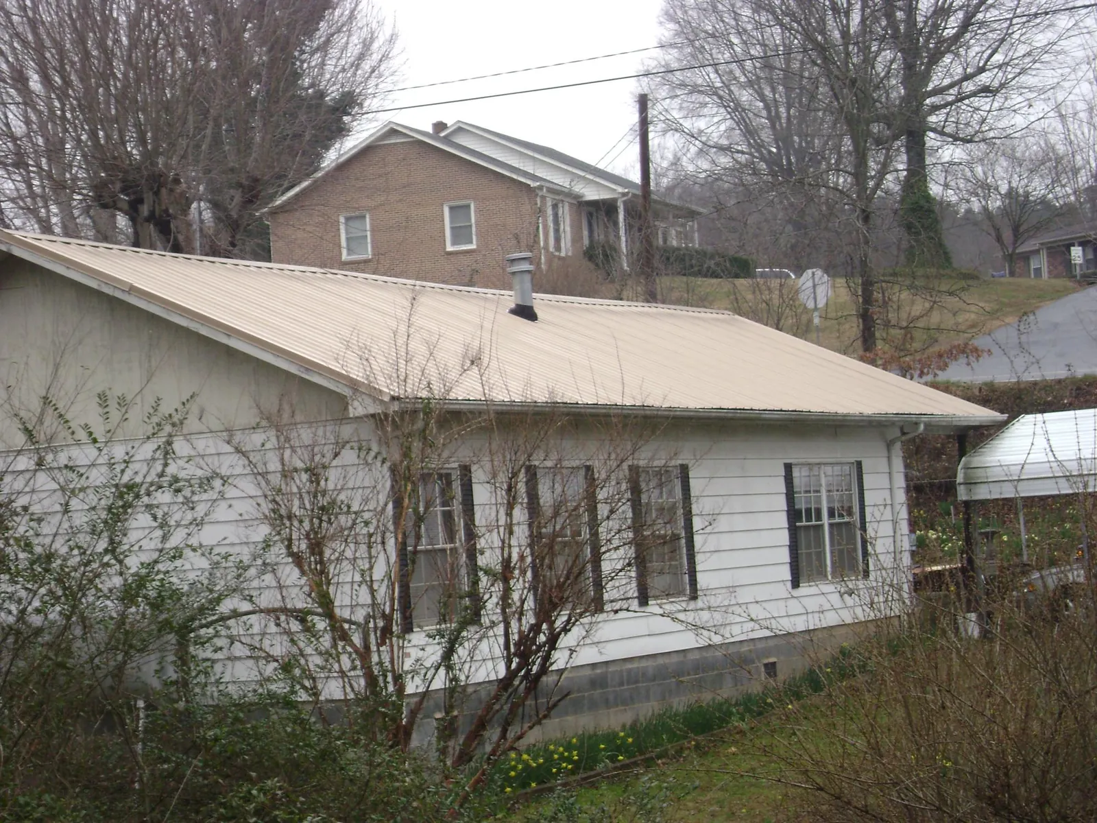 Tan metal roof on a white sided house set into a hillside — Commercial Roofing by Roofing Brothers in South Thomaston
